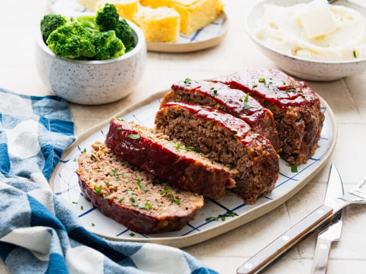 Horizontal side shot of Southern meatloaf on a table with a side of cornbread, mashed potatoes, and broccoli.