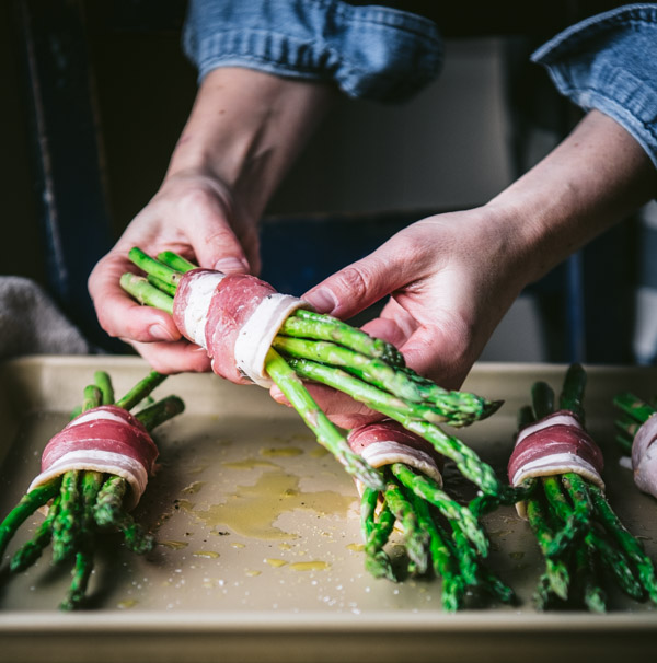 Process shot showing how to wrap asparagus bundles with bacon