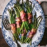 Overhead shot of hands holding a serving tray full of the best bacon wrapped asparagus recipe