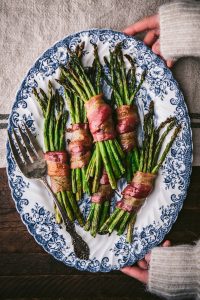 Overhead shot of hands holding a serving tray full of the best bacon wrapped asparagus recipe