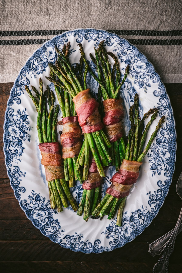 Platter of bacon-wrapped asparagus on a wooden dinner table