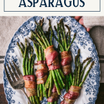 Hands holding a tray of bacon wrapped asparagus with text title box at top