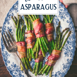 Hands holding a platter of bacon wrapped asparagus with text title overlay