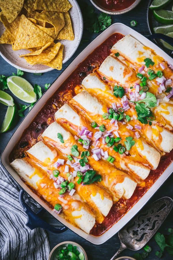 An overhead image of a casserole dish filled with freshly baked beef and cheese enchiladas, served with chips and salsa.