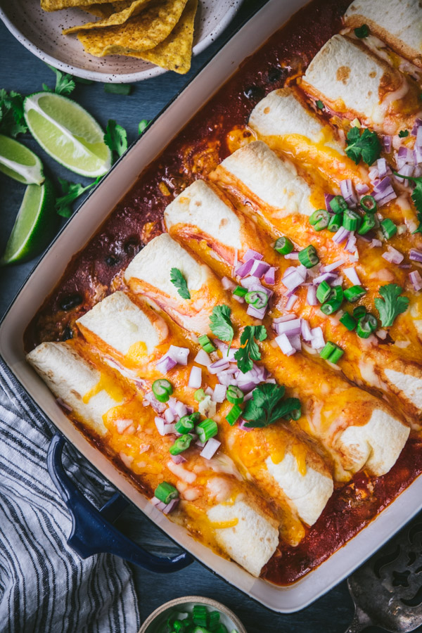 Close overhead image of ground beef enchiladas on a table with chips, salsa, and rice