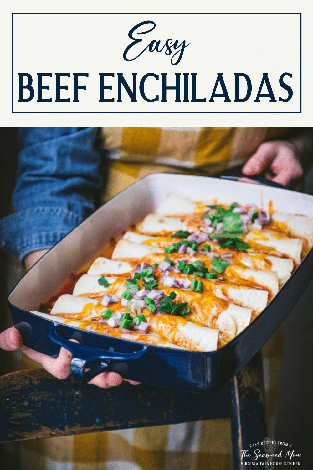Hands holding a pan of the best beef enchilada recipe with text title box at top