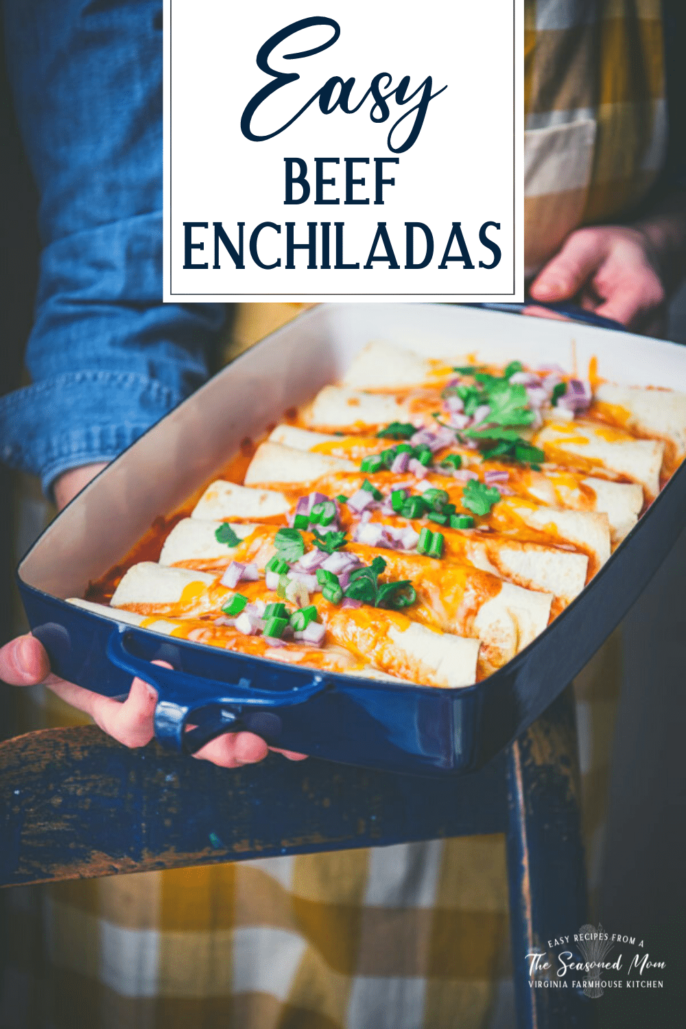 Hands holding beef enchiladas in a blue baking dish with text title overlay