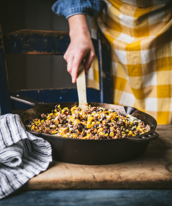 A woman mixed ground beef, corn, and beans in a skillet to make enchilada filling.