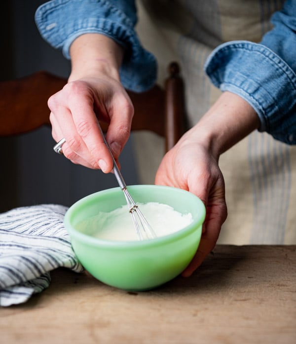 Whisking mayonnaise and sour cream dressing in a small green bowl