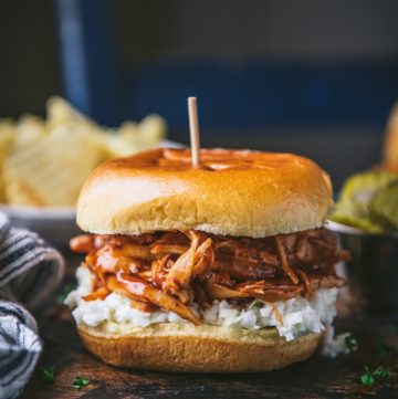Side shot of a crockpot bbq chicken sandwich with a side of potato chips and coleslaw