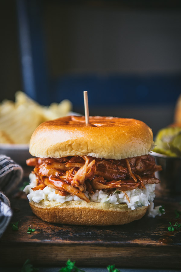 BBQ chicken sandwich on a wooden board with coleslaw and pickles