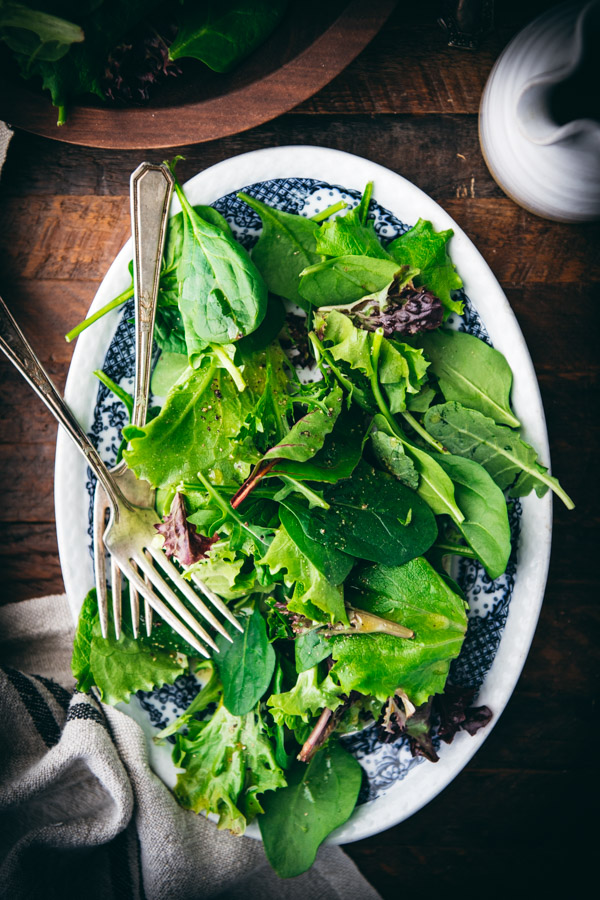 Simple green salad dressed with mustard vinaigrette on a blue and white platter