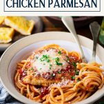 Close up side shot of a bowl of crispy fried and baked chicken parmesan served with spaghetti, bread, and salad and text title box at top.