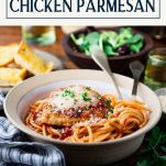 Side shot of chicken parmesan recipe on a dinner table with text title box at top