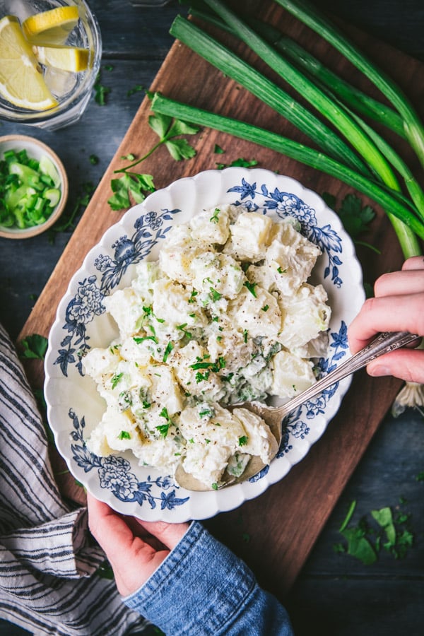 Hands serving an easy potato salad recipe from a blue and white bowl
