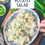 Overhead shot of hands serving easy potato salad recipe with text title box at top