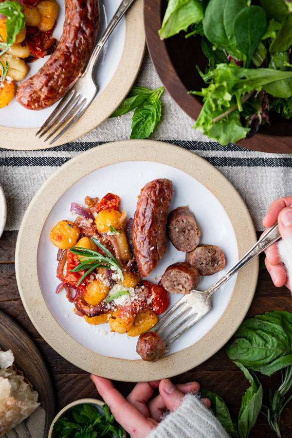 Overhead shot of hands eating a plate of sheet pan gnocchi with sausage with a fork