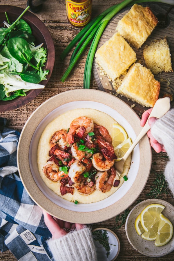Overhead shot of hands eating a bowl of shrimp and grits