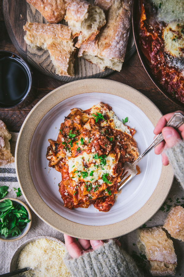 Overhead shot of hands eating an easy lasagna recipe from a white bowl