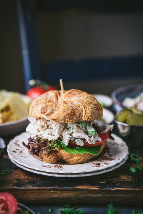 Side shot of a chicken salad sandwich on a croissant with potato chips in the background