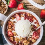 Close overhead shot of a bowl of strawberry crisp on a wooden table