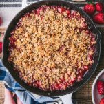 Hands holding a warm strawberry crisp in a white cast iron skillet