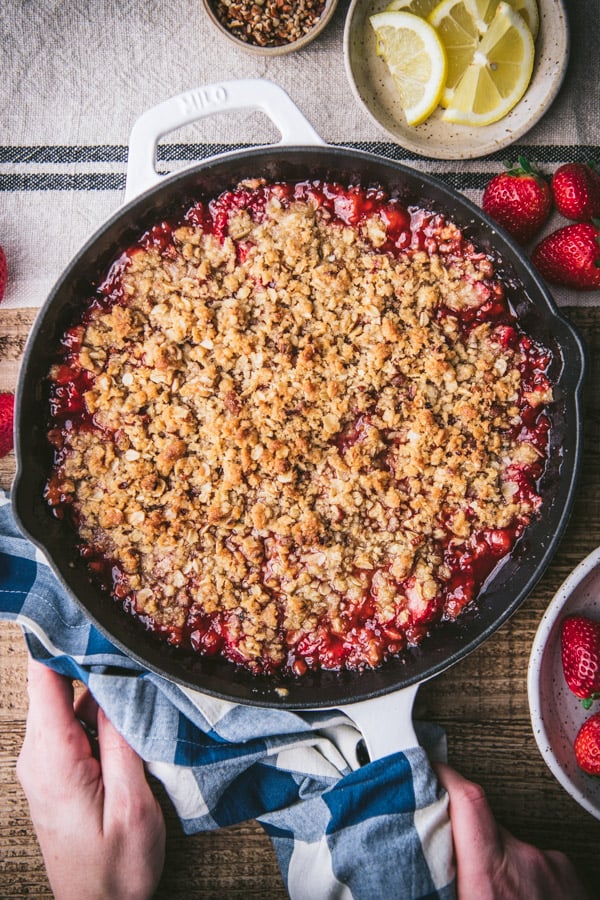Hands holding a warm strawberry crisp in a white cast iron skillet