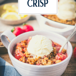 Side shot of a bowl of strawberry crisp with vanilla ice cream and text title overlay