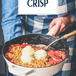 Hands holding a skillet of the best strawberry crisp recipe with text title overlay