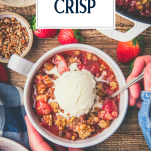 Overhead shot of hands eating a bowl of strawberry crisp with text title overlay