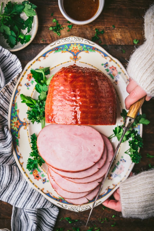 Overhead shot of hands holding a baked ham with apricot glaze on a platter