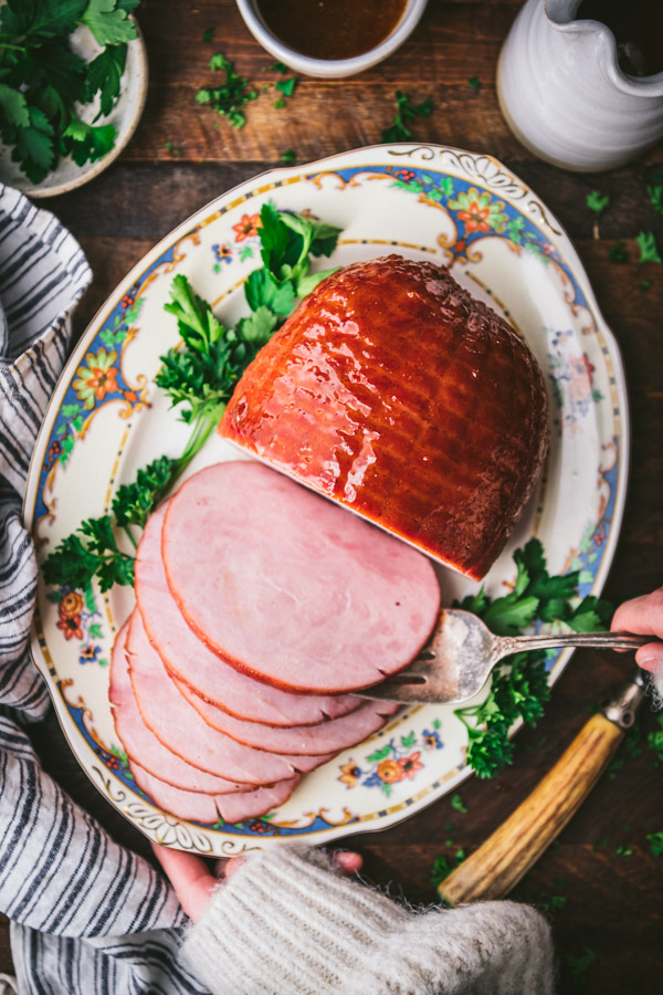 Hands serving a glazed ham on a platter