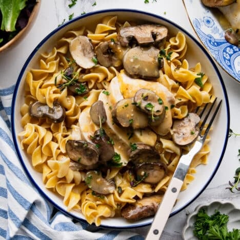 Square overhead shot of a bowl of baked chicken marsala served over noodles.
