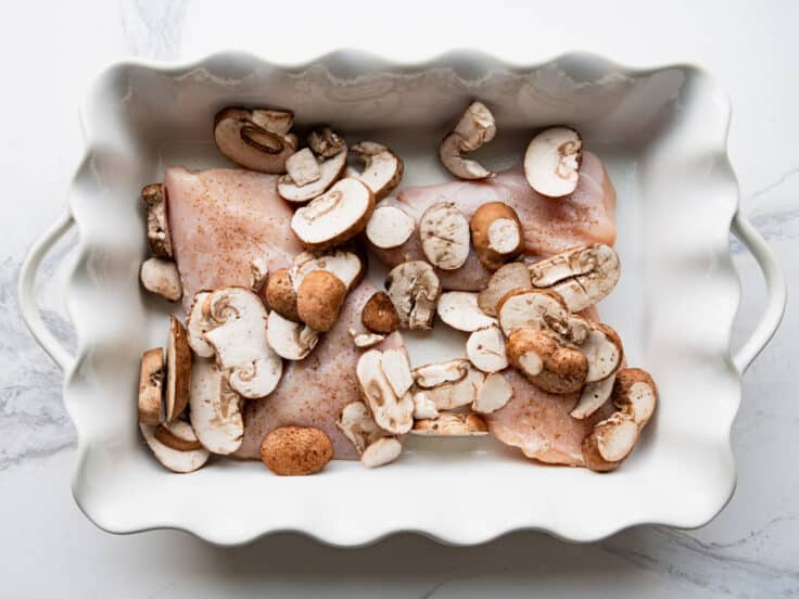 Chicken cutlets and sliced mushrooms in a baking dish.