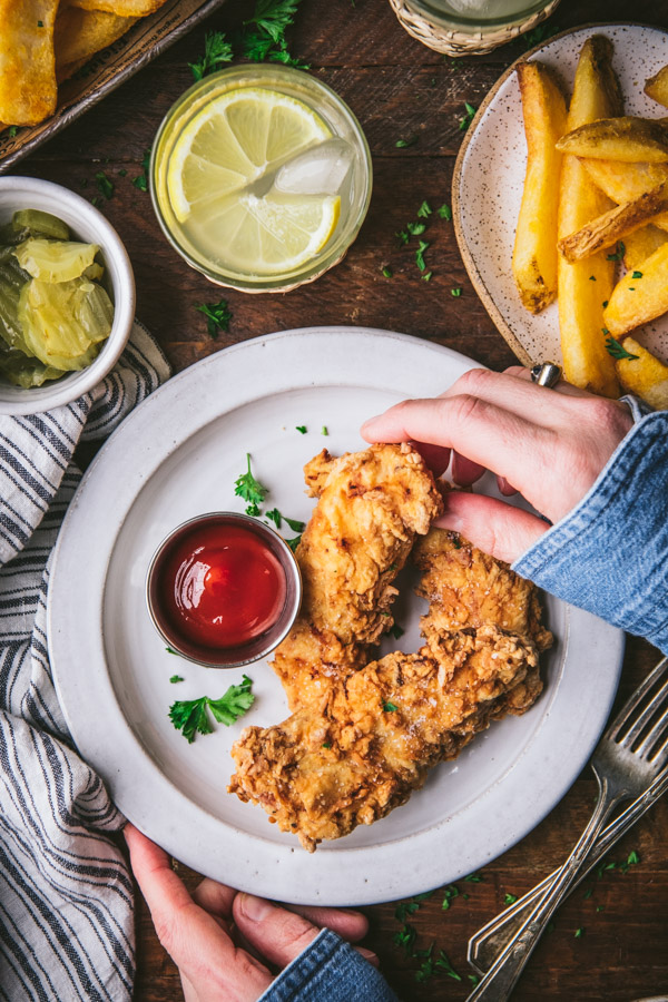 Hands eating the best fried chicken tenders recipe from a white plate
