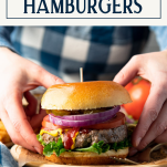 Hands holding grilled hamburger recipe with text title box at top