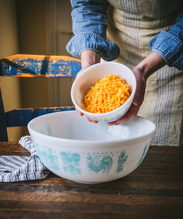 Adding grated cheddar cheese to a mixing bowl