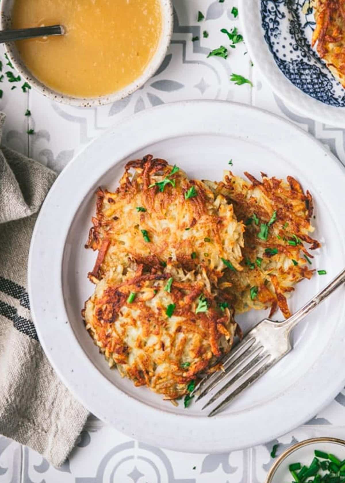 Close overhead image of a white plate full of three potato pancakes with fresh chives on top.