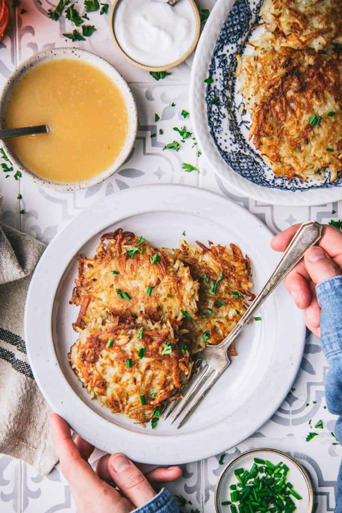 Overhead image of hands eating potato pancakes with a side of applesauce.