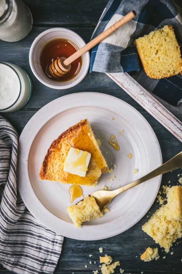 Overhead shot of a piece of sweet cornbread on a plate with butter and honey