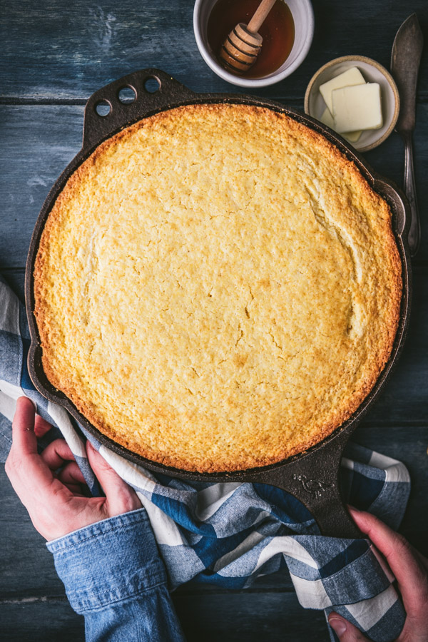 Overhead shot of hands holding a cast iron skillet of sweet cornbread