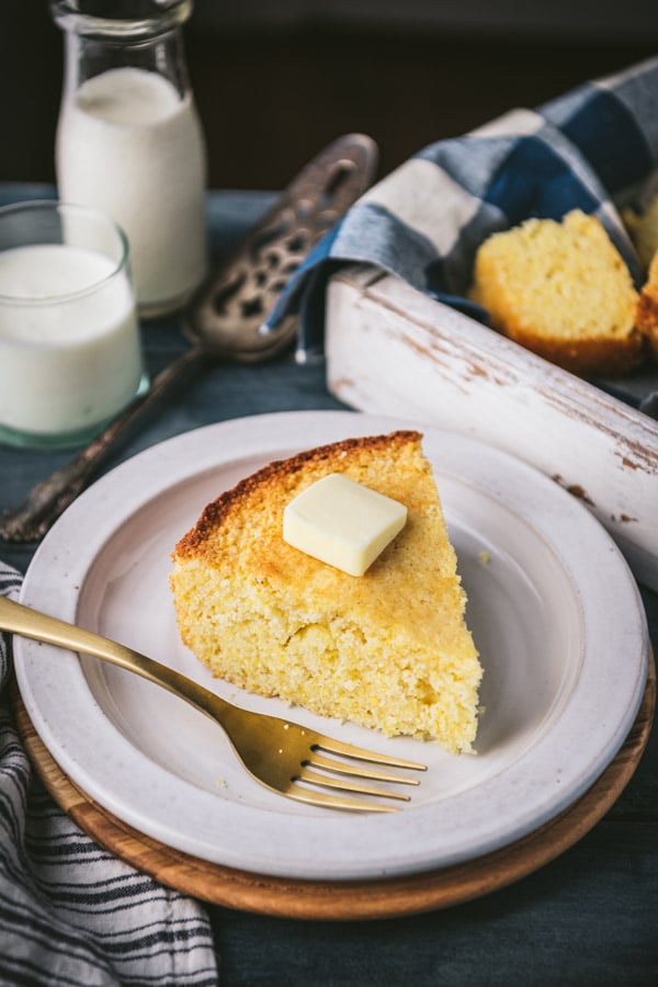 Side shot of a slice of sweet cornbread on a white plate with butter on top