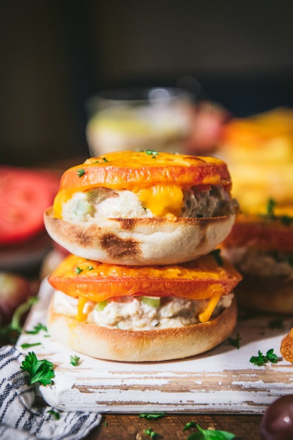 A classic tuna melt made on two halves of an English muffin, stacked on top of each other. The melt has a slice of tomato and melted cheese on each half.