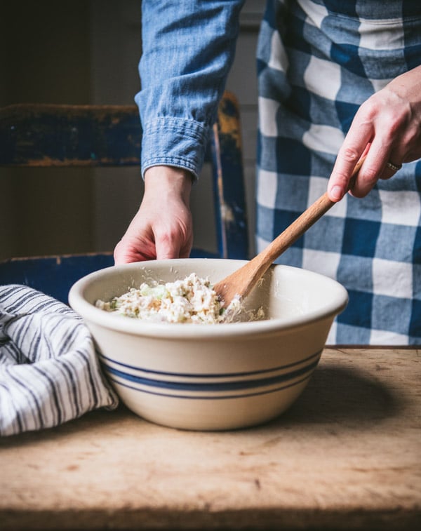 A woman stirs a large bowl of tuna salad with a wooden spoon.