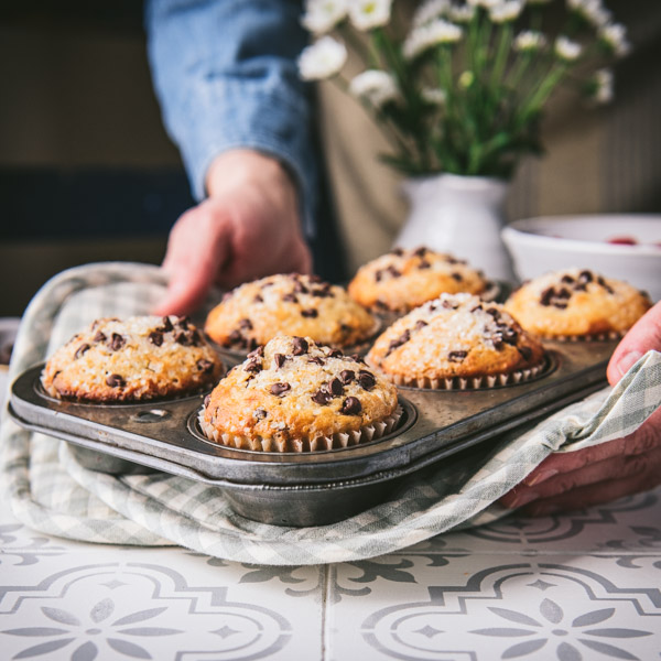Hands holding a muffin tin with gingham pot holders