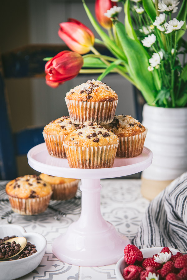 The best chocolate chip muffin recipe served on a pink cake stand on a table with tulips in the background