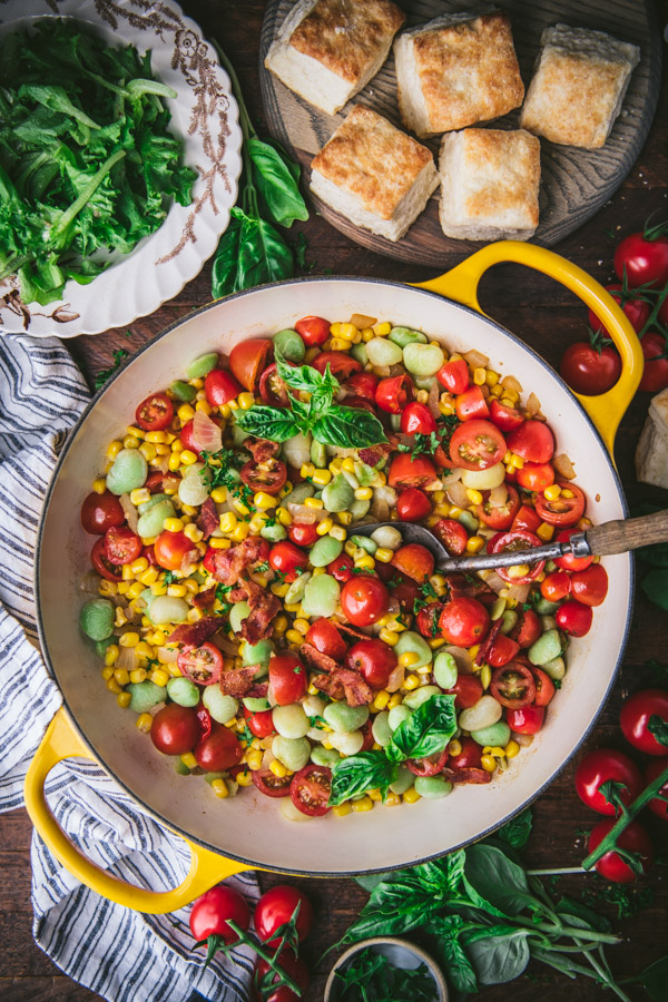 Overhead shot of a pan of the best southern succotash recipe on a table with a side of biscuits and salad