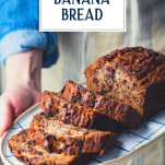 Hands holding a sliced loaf of chocolate chip banana bread on a plate with text title overlay