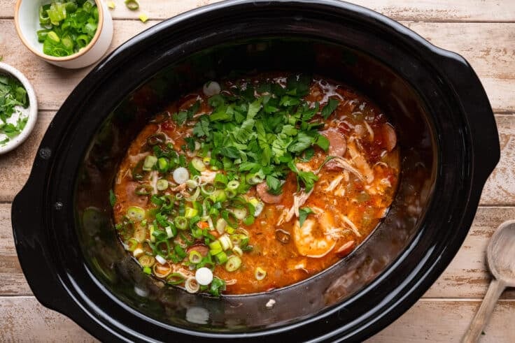 Adding green onions and herbs to a pot of slow cooker gumbo.