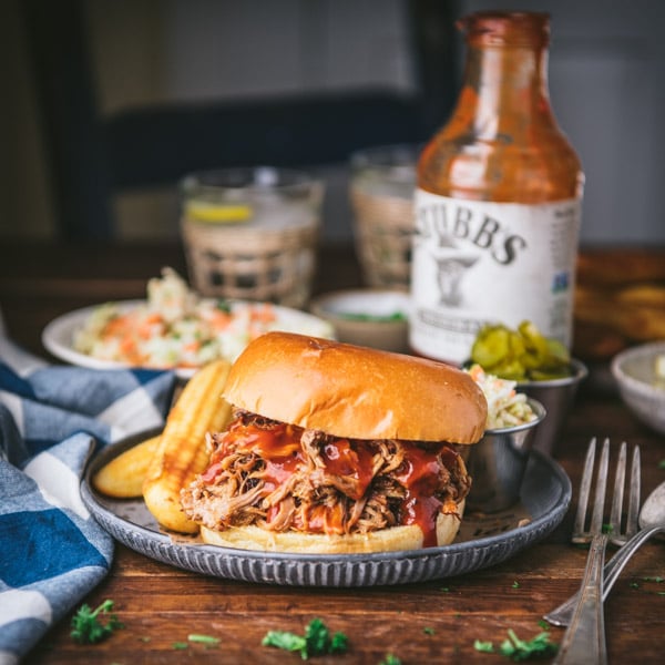 Square side shot of slow cooker pulled pork on a sandwich on a plate with cornbread and coleslaw